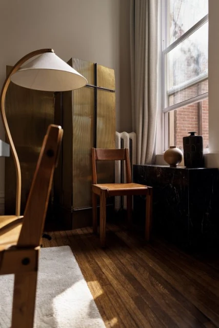 Interior view of room with chair, floor lamp, cabinet, marble-topped furniture piece, wooden floor and window with curtains. 