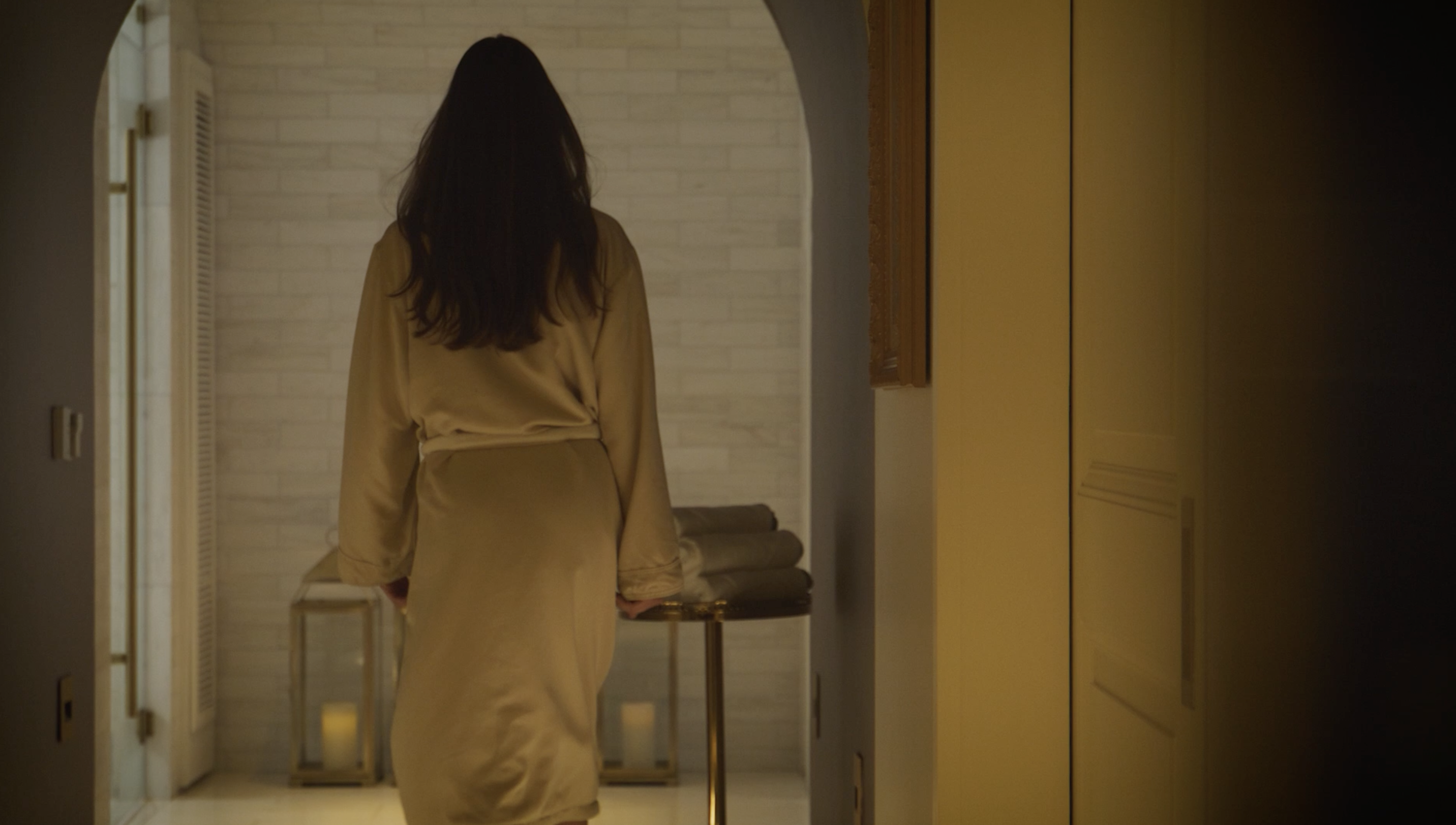 Woman in robe walks through hallway of spa. Neutral tones, soft lighting, luxurious setting. Relaxation and wellness concept, back view.
