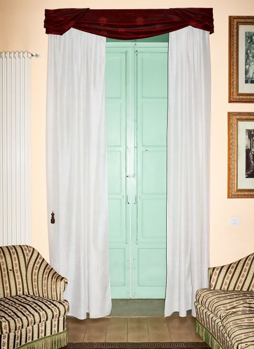 A doorway framed by white curtains and a decorative burgundy valance, with furniture on either side and art hanging on the wall.