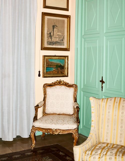 Interior with two upholstered armchairs, vintage framed artwork on the wall, mint green door, white curtains, and dark rug on the floor.