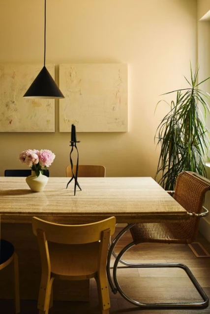 Interior dining room scene featuring a wooden table set with flowers and candle, surrounded by modern design chairs and neutral walls.