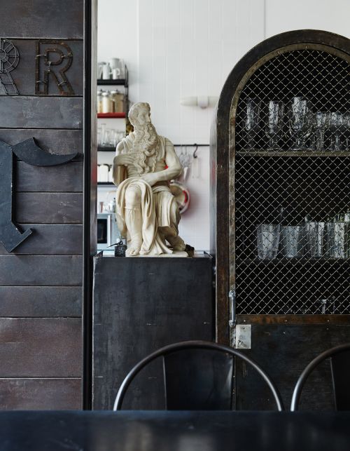 Interior shot with a statue of Moses, a metal cabinet, and decorative metal letters against a white wall in an indoor setting.