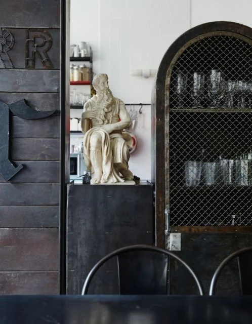 Interior shot with a statue of Moses, a metal cabinet, and decorative metal letters against a white wall in an indoor setting.