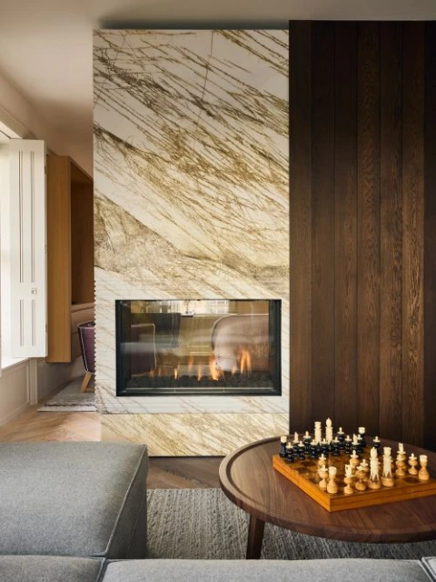 Living room interior with a modern fireplace with marble surround and a chessboard on a coffee table near a grey sofa.
