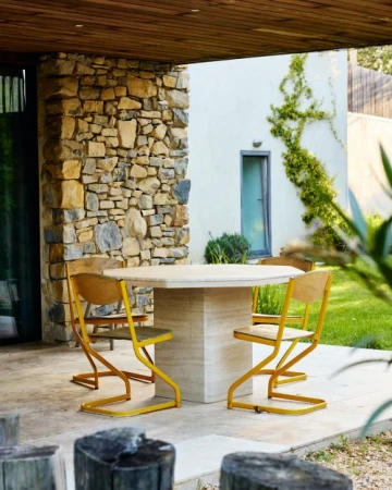 Octagonal stone dining table surrounded by yellow-framed chairs on a patio with a stone pillar and modern building exterior