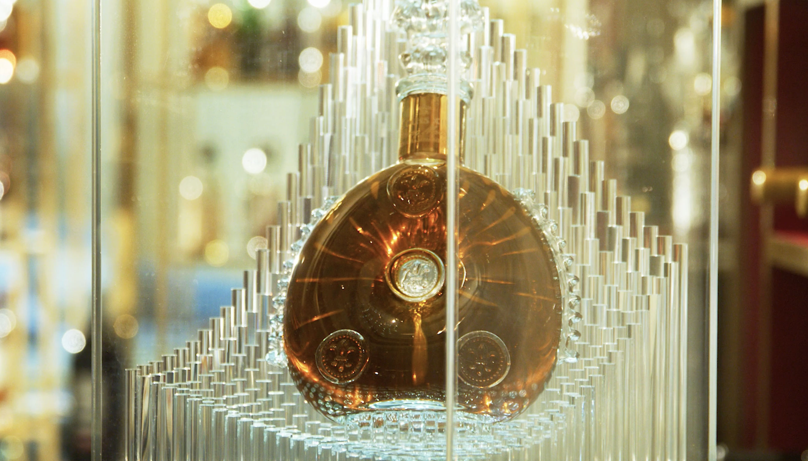 Decorative golden liquor bottle in a clear display case with an elaborate crystalline base, viewed in a close-up shot.