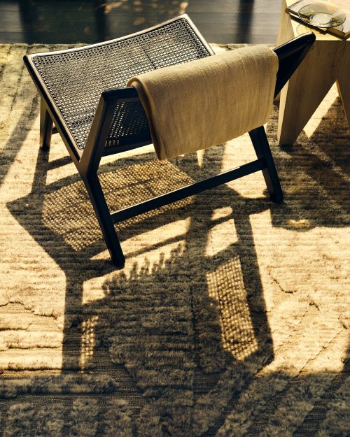 Wicker chair with a tan towel draped over the back, casting a shadow on the patterned rug beneath it in soft, diffused lighting.