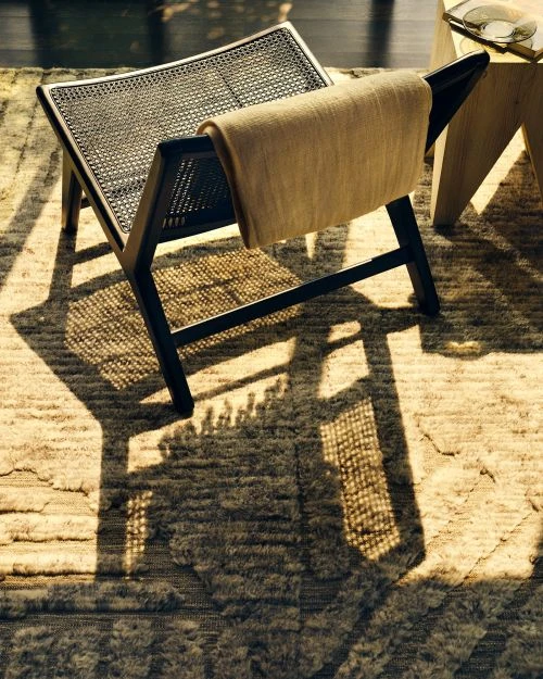 Wicker chair with a tan towel draped over the back, casting a shadow on the patterned rug beneath it in soft, diffused lighting.