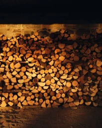 A neatly stacked pile of split firewood logs with visible circular end grain illuminated by warm light.