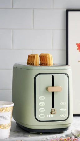 Sage green toaster with two waffles popping out against white tiled kitchen wall by Graydon Herriott