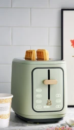 Sage green toaster with two waffles popping out against white tiled kitchen wall by Graydon Herriott