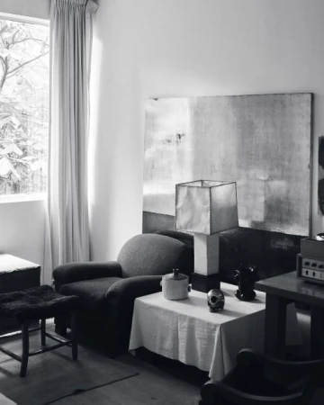 Monochrome interior photograph showing a living room with a table lamp and large abstract artwork by Graydon Herriott