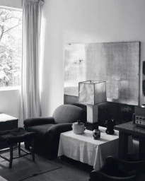 Monochrome interior photograph showing a living room with a table lamp and large abstract artwork by Graydon Herriott
