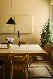 A minimal dining room with a marble table, wooden chairs, a vase of pink flowers, and a modern black pendant light.