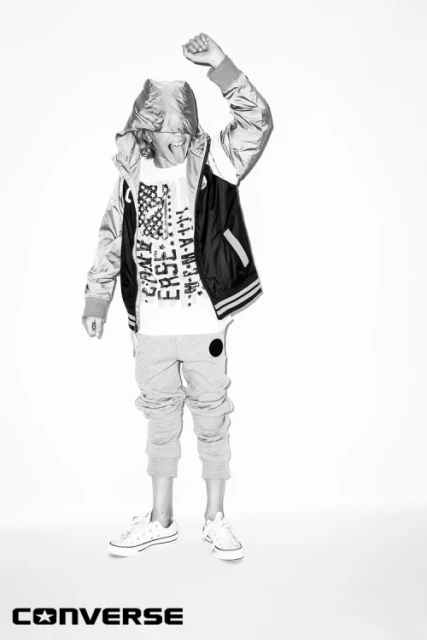 Youth fashion shot in black and white featuring a child model in streetwear, posing with an arm raised, sneakers, and Converse branding.