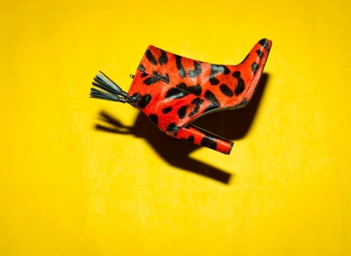 Red and black leopard print heeled ankle boot with tassels on a yellow background in a fashion studio setting.