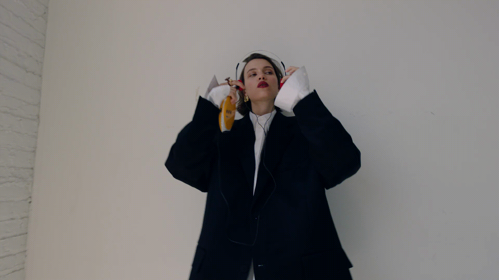 Woman in oversized blazer and headset holding yellow device. Bright studio lighting. Fashion, music, and lifestyle visuals.