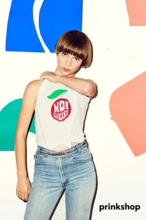 A young woman poses in a white tank top and blue jeans against a colorfully painted backdrop. Fashion and lifestyle portrait.