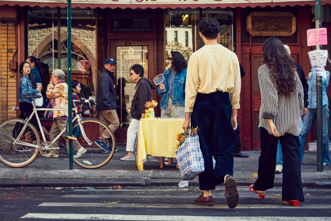 People walking on a city street with a bicycle parked nearby, an outdoor scene with vendors and pedestrians in the background.