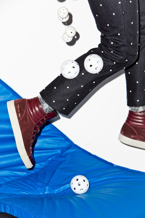 Legs wearing black and white polka-dot pants and burgundy hi-top sneakers jumping over a blue inflatable with several white perforated balls.