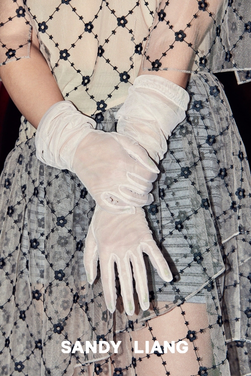 Close-up of hands wearing sheer white gloves crossed over a patterned mesh skirt with black floral details.