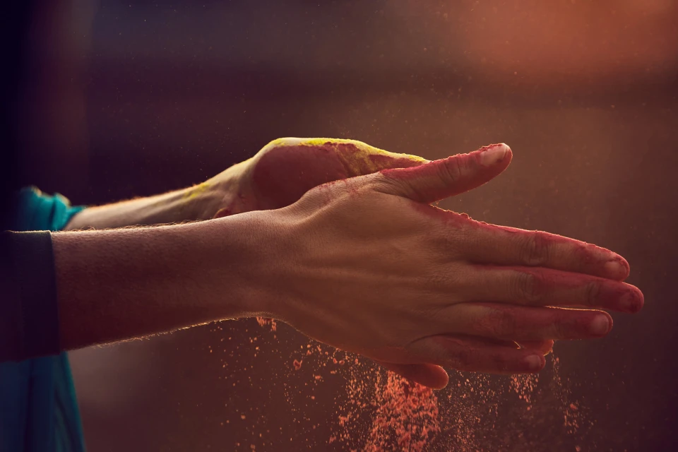 Close-up of a person's hands covered in colorful powder, possibly participating in a Holi festival celebration, against a dark background.