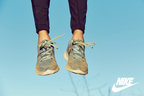 Close-up of a person's legs and feet wearing knit sneakers and dark trousers against a clear blue sky background