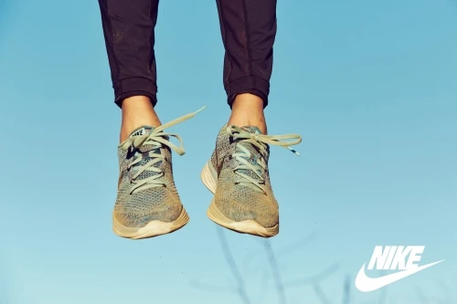 Close-up of a person's legs and feet wearing knit sneakers and dark trousers against a clear blue sky background