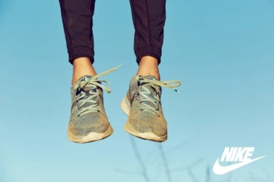 Close-up of a person's legs and feet wearing knit sneakers and dark trousers against a clear blue sky background