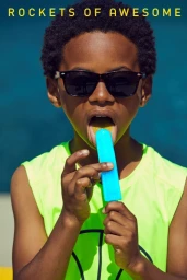 Young Black child wearing black sunglasses and a lime green sleeveless top, licking a bright blue ice pop.