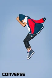Young person wearing a red and blue jacket leaping against a plain blue background by Meredith Jenks