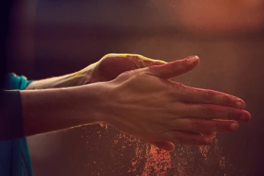 Close-up of hands clapping together with red and yellow powder dust scattering into the warm air