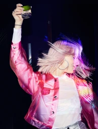 Woman in shiny pink jacket raising a glass with lime against a dark nightlife background