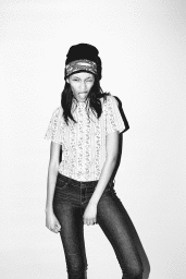 Young woman wearing a beanie and patterned t-shirt posing playfully against a white wall