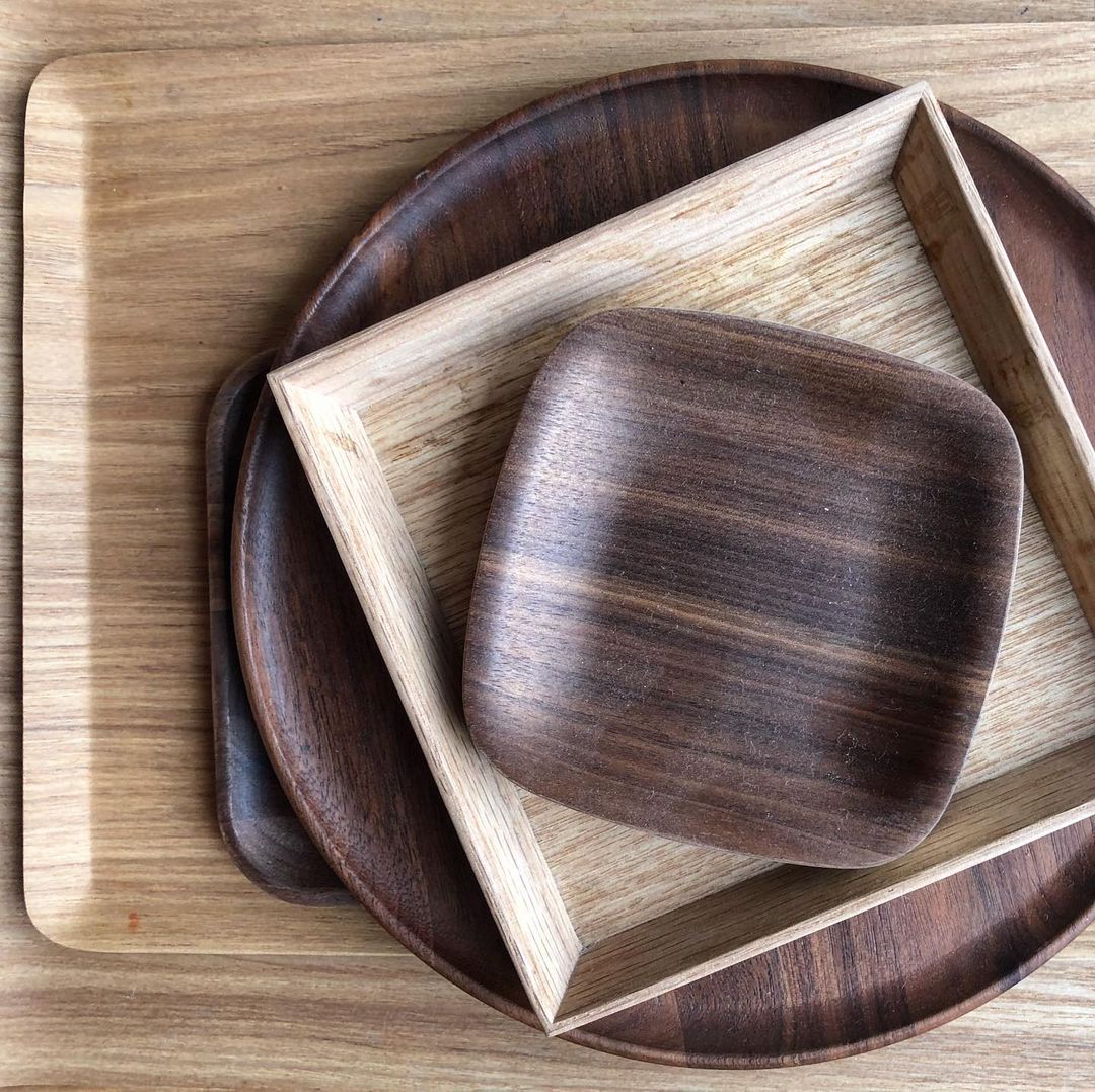 Overhead shot of stacked wooden trays in varying shapes including round, square, and rectangular, showcasing wood grain textures.