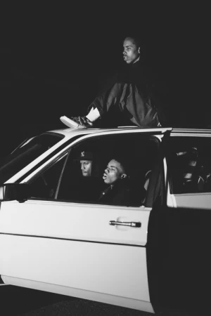 Monochrome portrait of three men with one sitting on top of a car and two seated inside by photographer Joyce Kim