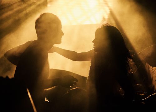 Silhouette of a man and a woman in a dimly lit room, sharing an intimate moment, backlit by a bright light source.