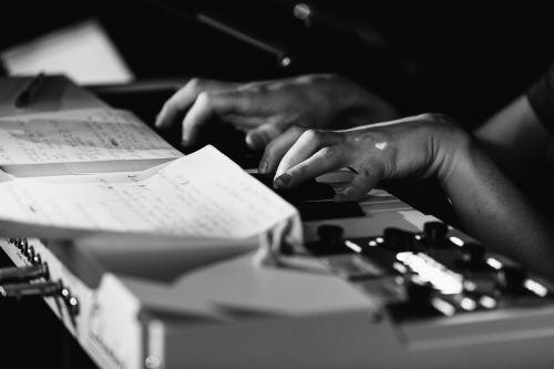 Hands playing an electric piano with sheet music in black and white, creating a strong contrast between light and shadow.