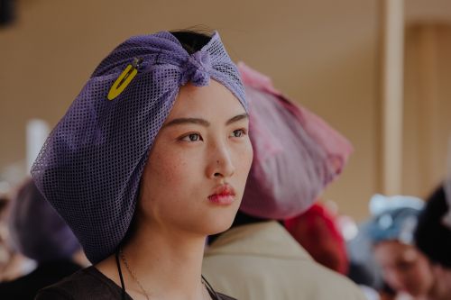 Asian woman with hair wrapped in a purple net, featuring a yellow clip, looking off to the side in a softly lit indoor setting.