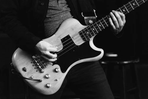 Monochrome photo of a person playing an electric bass guitar, with a stool in the background, capturing the essence of music performance.