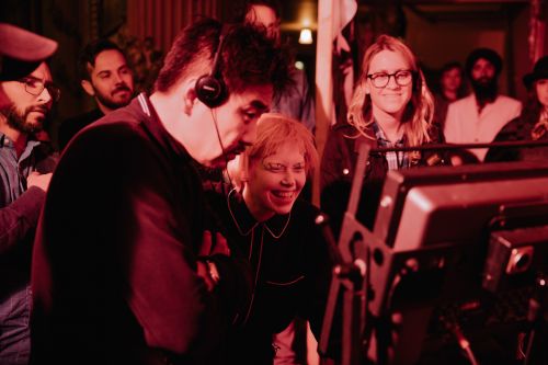 Candid image of a diverse group of adults around camera equipment, bathed in red lighting, during a film or video production.