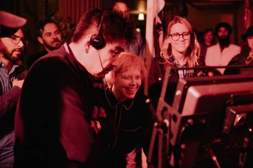 Candid image of a diverse group of adults around camera equipment, bathed in red lighting, during a film or video production.