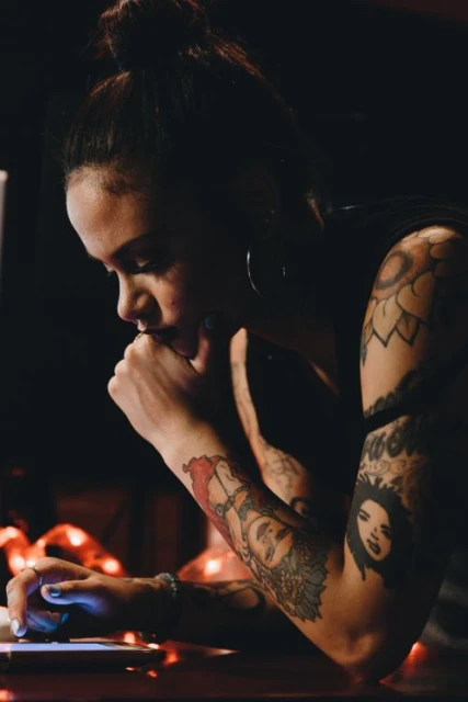 Portrait of a young adult woman with tattoos looking at her smartphone. The woman is illuminated by the light from the smartphone screen.