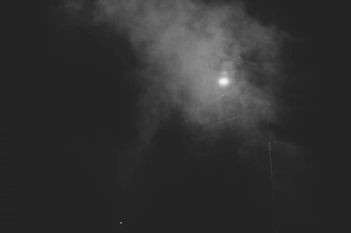 Monochromatic image capturing a bright street lamp emitting rays through the misty atmosphere at night.