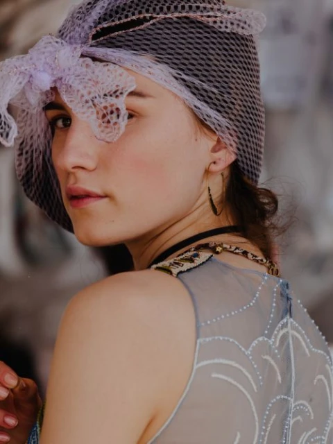 Close-up portrait of a fair-skinned young woman wearing a net head covering, looking over her shoulder in front of a blurred background.