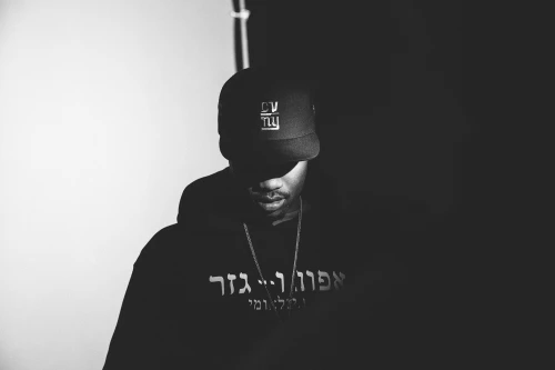 Monochrome portrait of a man wearing a black hoodie and a baseball cap with low-key studio lighting