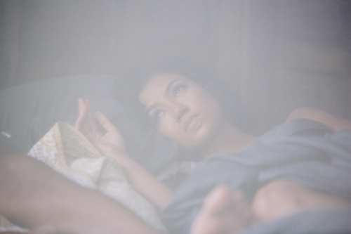 Woman lying in bed resting her head on a pillow under soft lighting with a hazy atmosphere
