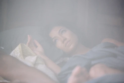 Woman lying in bed resting her head on a pillow under soft lighting with a hazy atmosphere