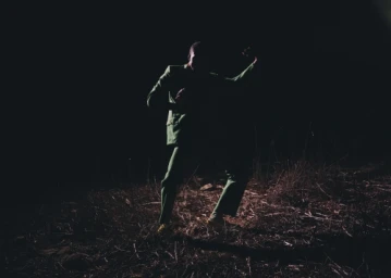 Man wearing a green suit dancing in a dark outdoor landscape at night photographed by Joyce Kim.