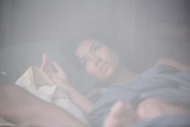 Woman lying in bed resting her head on a pillow under soft lighting with a hazy atmosphere